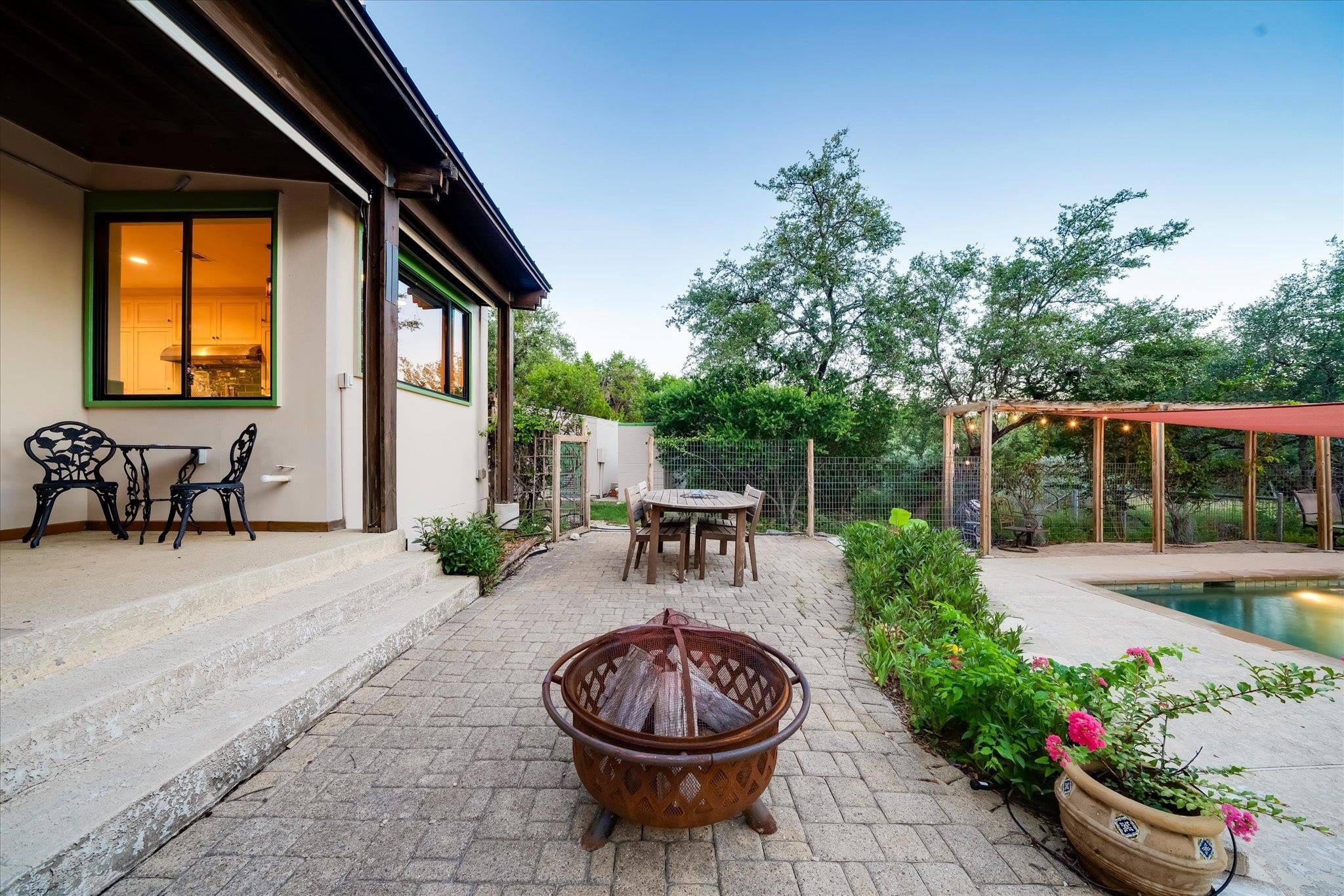 Iron fire pit on the paver patio outside 8300 Lime Creek Road, with the pool cabana and pool visible through a wire fence beyond