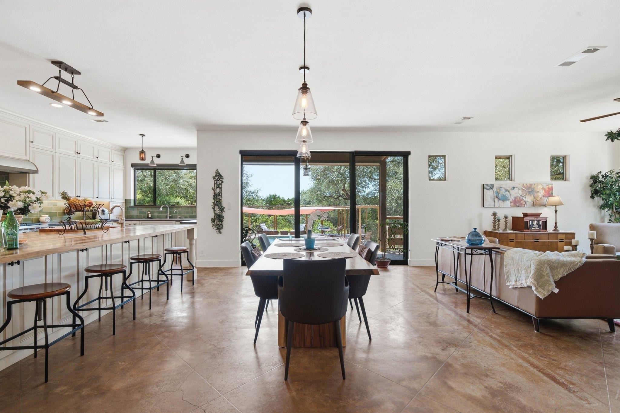 Great room interior at 8300 Lime Creek Road looking from the kitchen bar toward the dining table, sliding glass doors, and living room with a long stained concrete floor