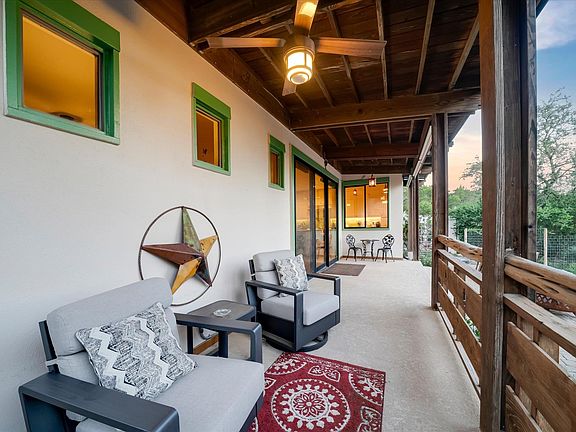 Covered cedar-ceiling porch at 8300 Lime Creek Road with green-trimmed windows, a Lone Star wall hanging, upholstered chairs and a small red patterned rug