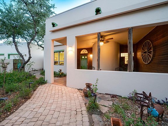 Stucco entry portico at 8300 Lime Creek Road with a wooden wagon-wheel wall detail, brick paver path, and mesquite planted alongside